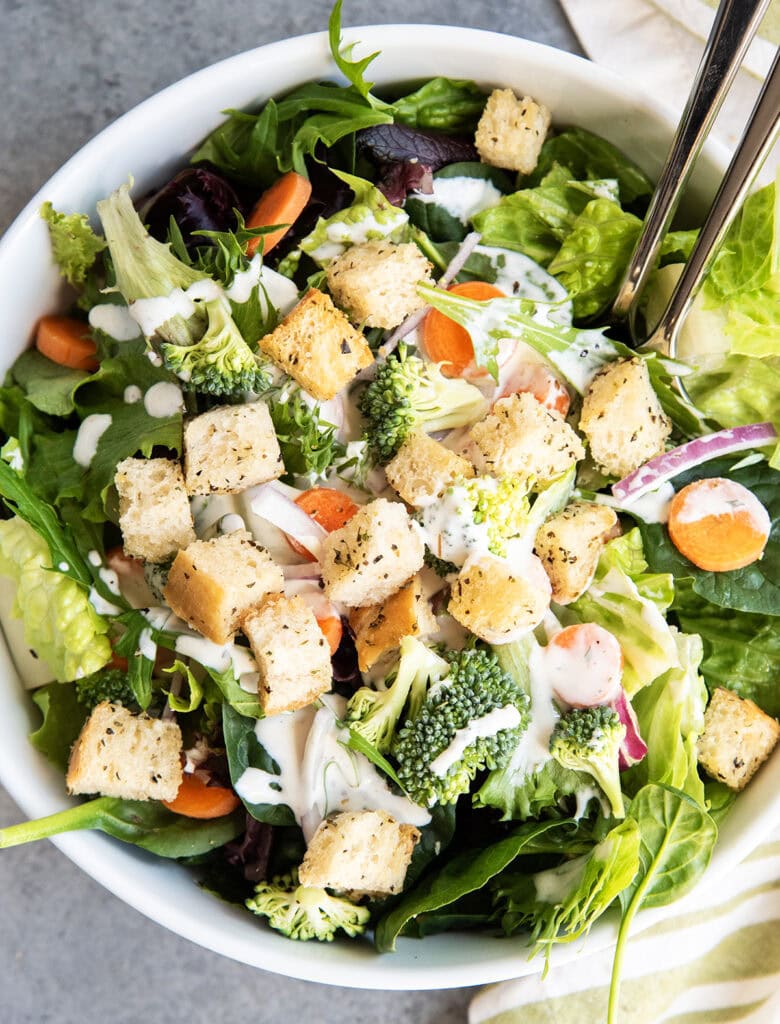 A salad topped with croutons, carrots, red onions, and ranch.
