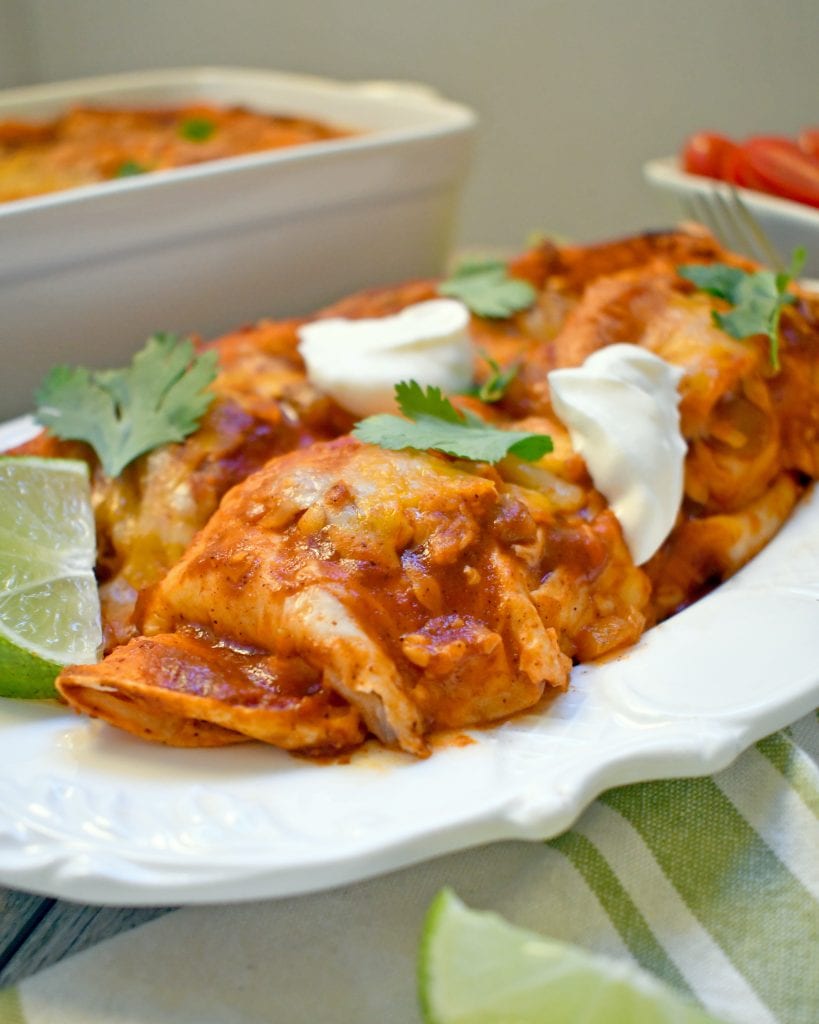 Angled view of slow cooker pork enchiladas on a white plate.