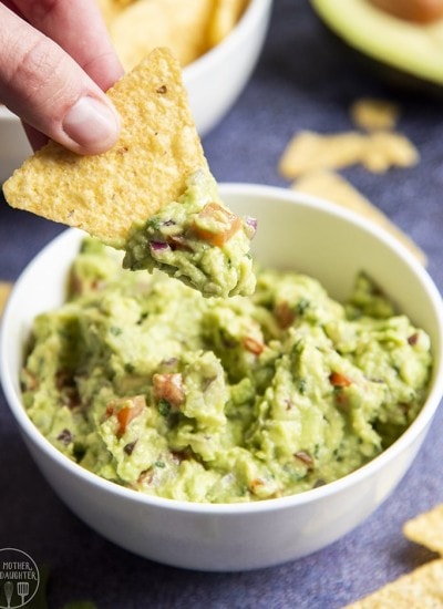 Close up image of Guacamole in a bowl with a hand chipping a dip into it