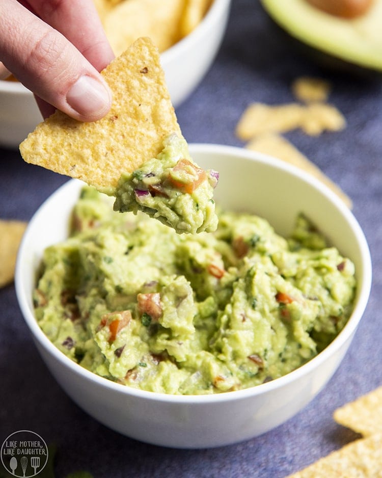 Close up image of Guacamole in a bowl with a hand chipping a dip into it