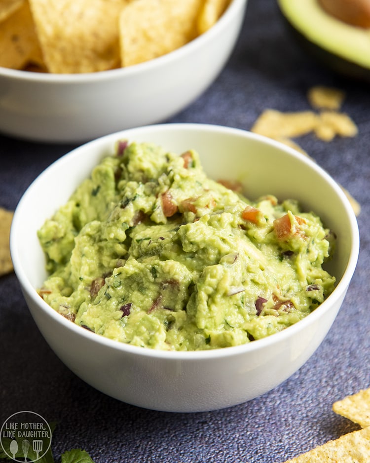 Close up image of Guacamole in a bowl with chips behind it