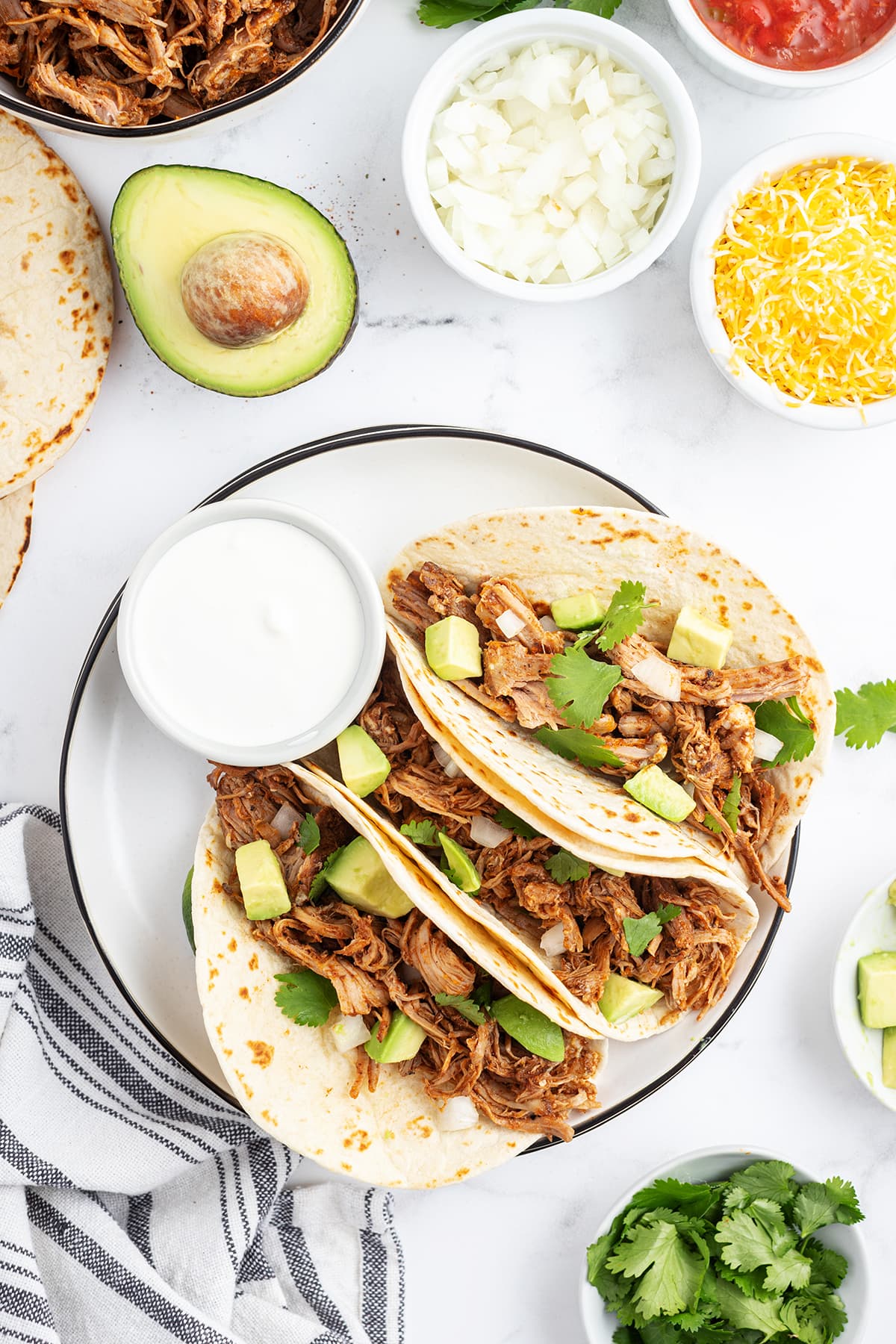 A plate of three pulled pork tacos topped with avocado and cilantro.