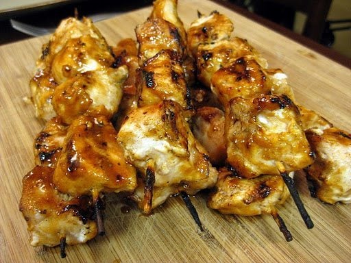 Angled view of chicken kebabs with sweet peanut sauce on a wood board.