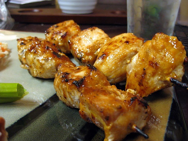 Angled view of chicken kebabs with sweet peanut sauce on a plate.