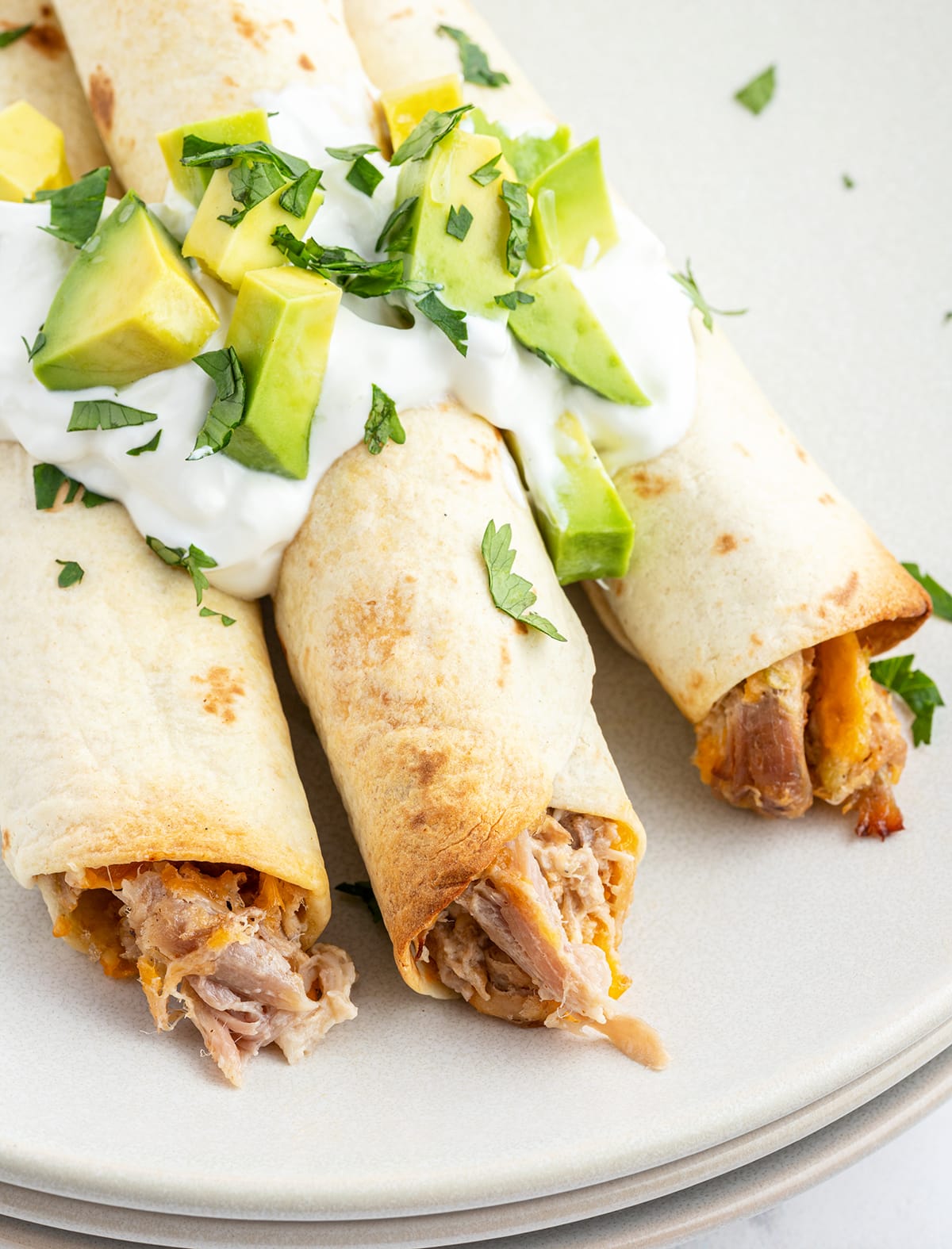 A close up of three pulled pork taquitos on a plate.