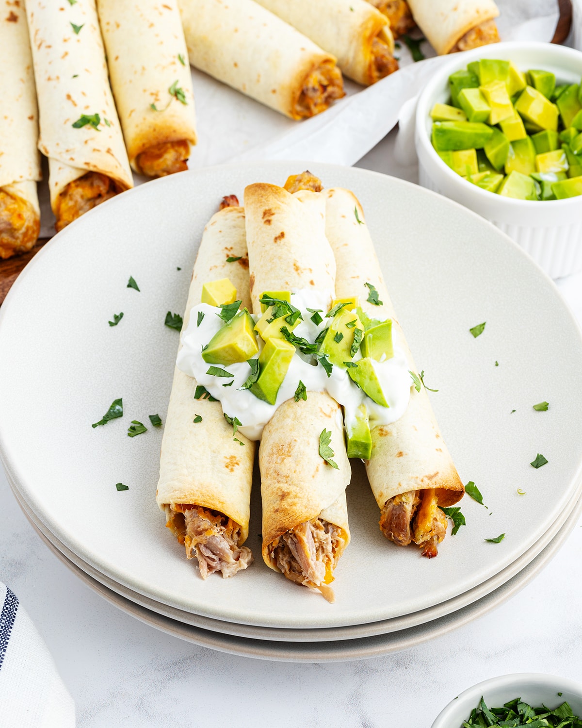 A plate of creamy pulled pork taquitos topped with sour cream and avocado pieces.