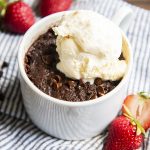 Brownie in a mug with vanilla ice cream on top on a striped cloth