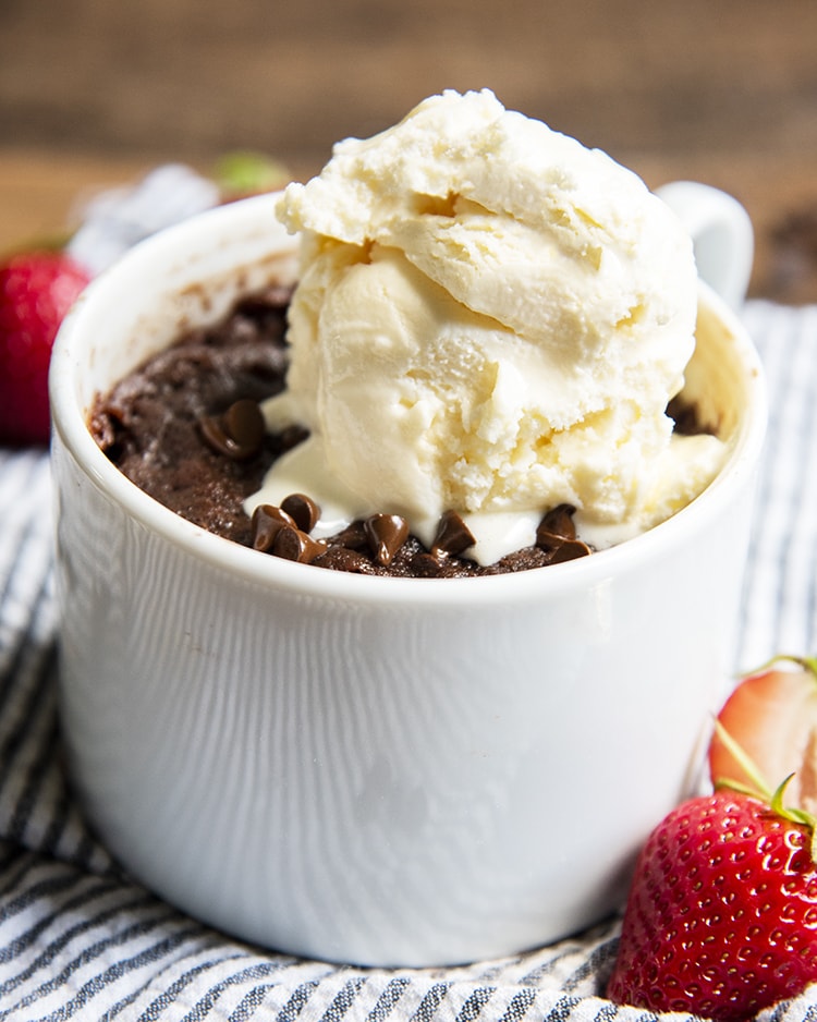 A chocolate brownie in a mug with vanilla ice cream melting on top