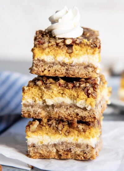 A stack of three pecan pumpkin cheesecake bars topped with a dollop of whipped cream.