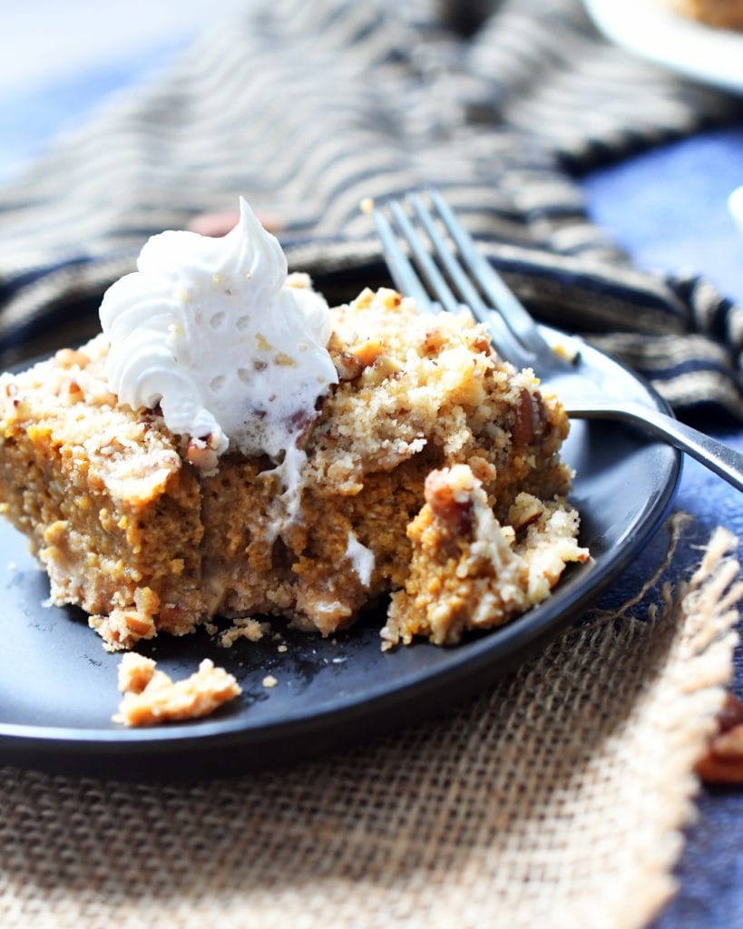 pecan pumpkin cheesecake bar topped with whipped cream on a brown plate with a fork next to it