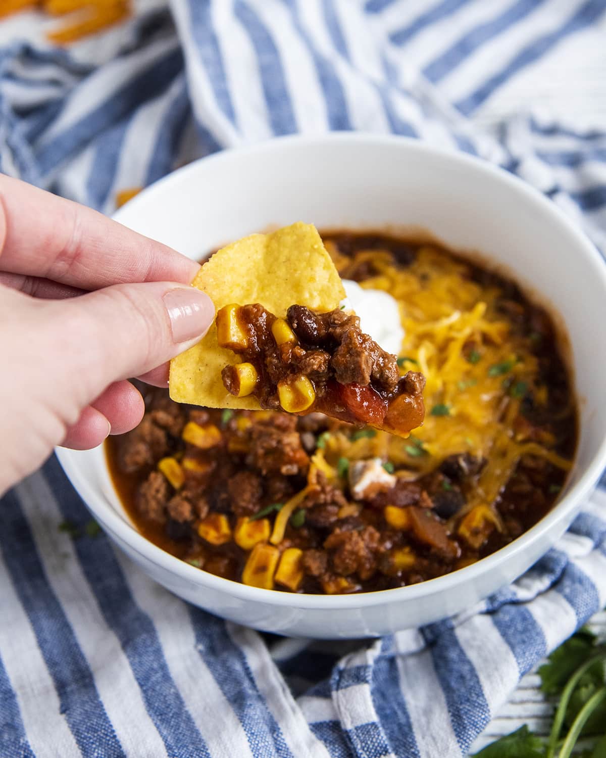 A hand holding a tortilla chip with taco soup on it.