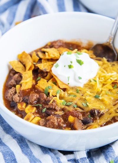 A close up of a bowl of taco soup topped with shredded cheese, tortilla strips, and sour cream.