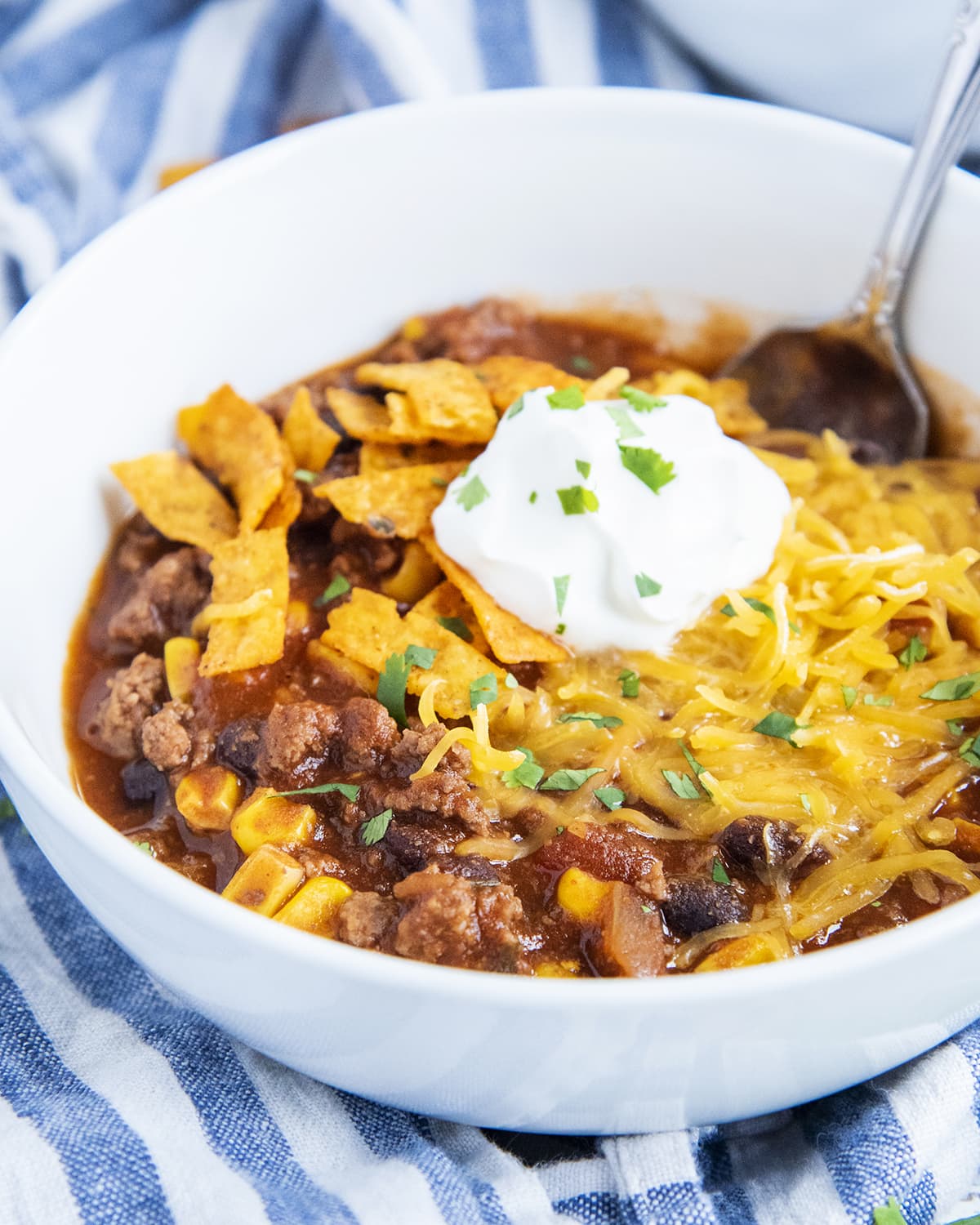 A close up of a bowl of taco soup topped with shredded cheese, tortilla strips, and sour cream.