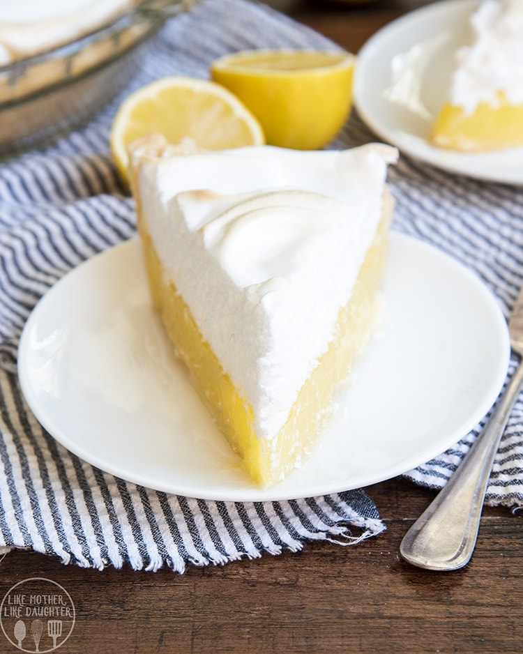 A slice of lemon meringue pie on a white plate, the bottom half is a yellow lemony curd filling topped with a thick white meringue topping.