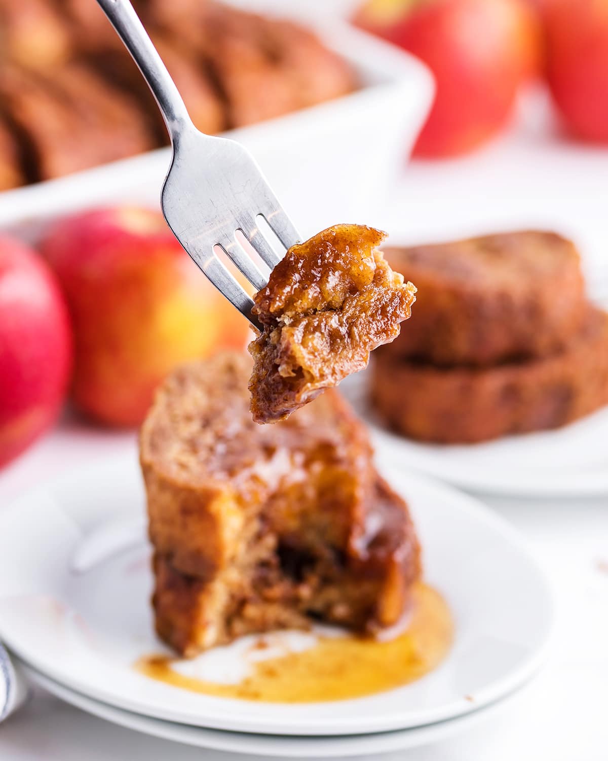 A bite of apple butter french toast on a fork with the dish in the background.