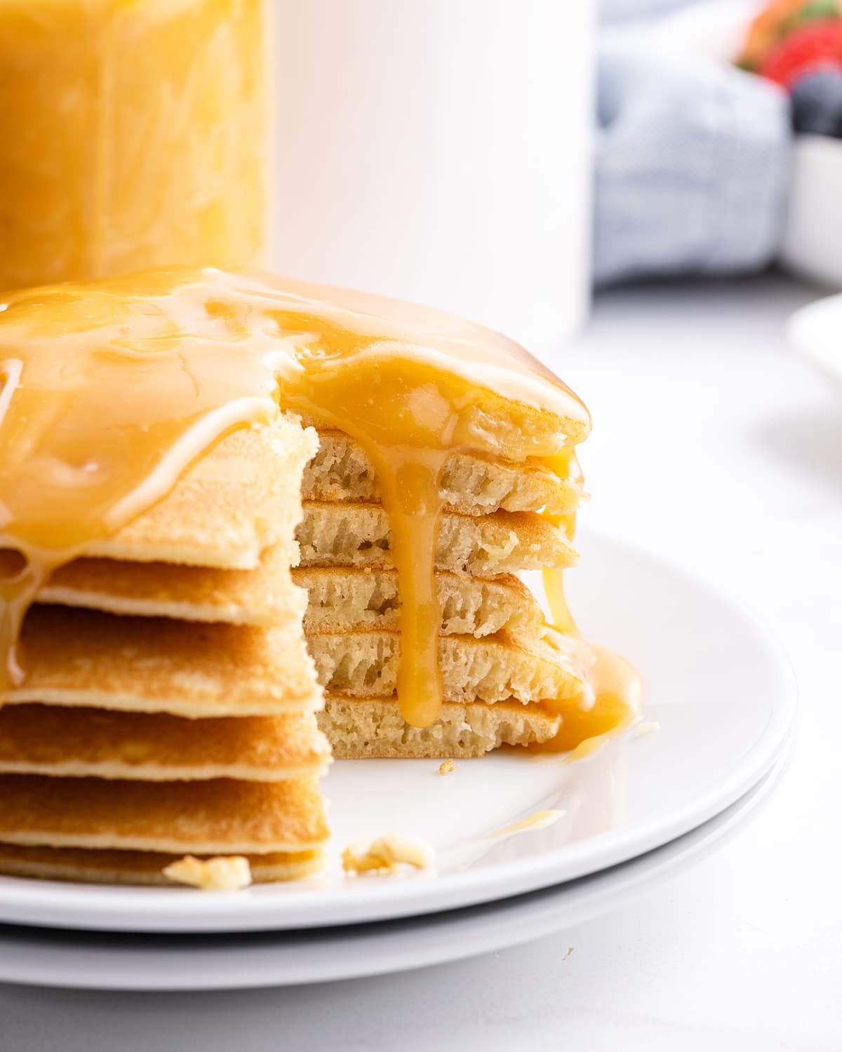 A stack of pancakes with buttermilk syrup on top, with bites cut out showing the middle of the pancakes.