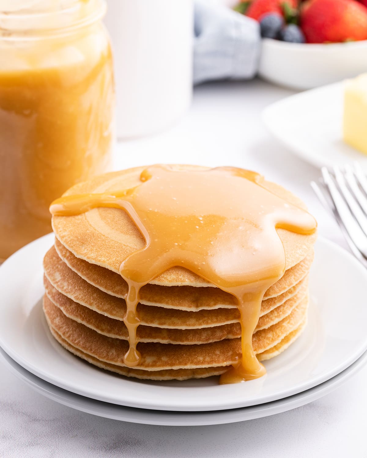 A stack of pancakes topped with a golden colored buttermilk syrup.