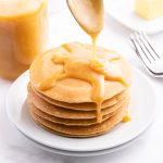 Buttermilk syrup being poured over a stack of pancakes off a spoon.