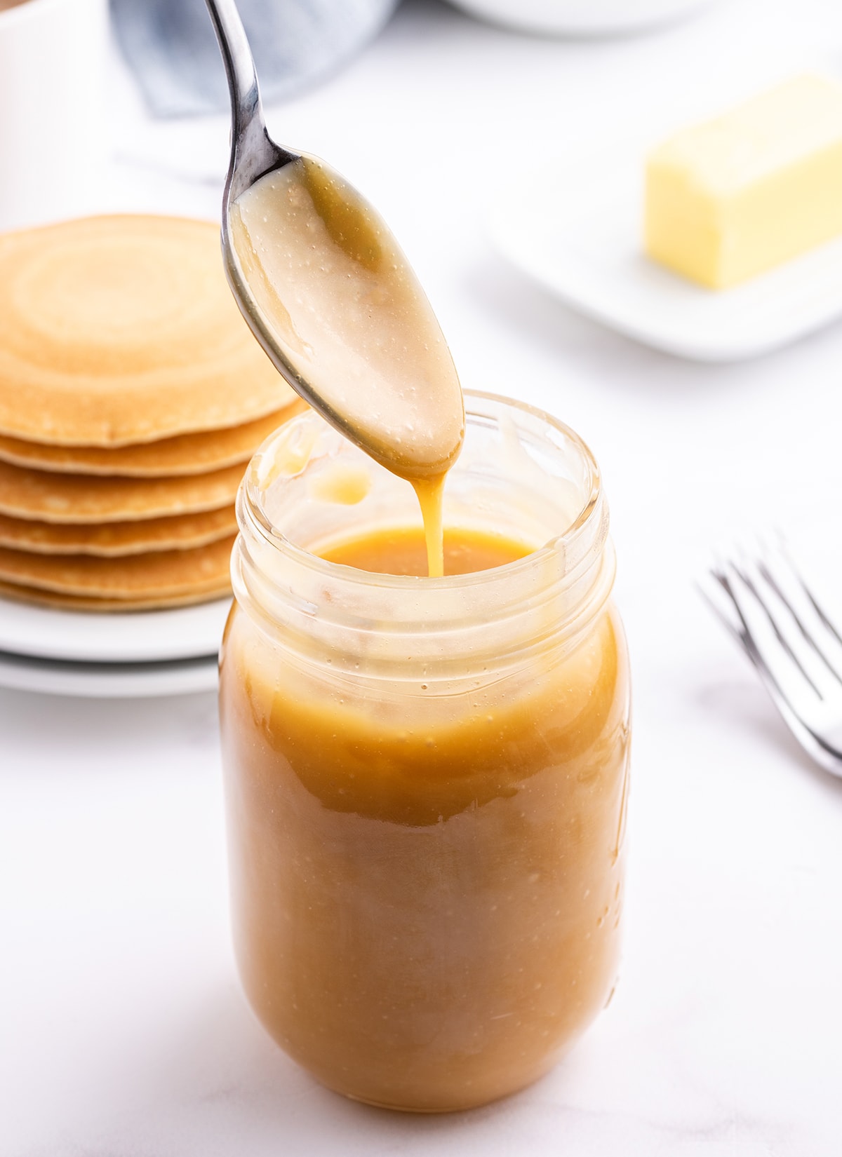 A spoon drizzling buttermilk syrup above a jar of it.