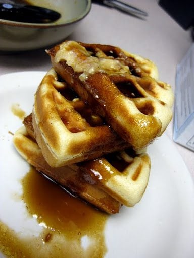 Close up view of cinnamon roll waffles on a white plate.