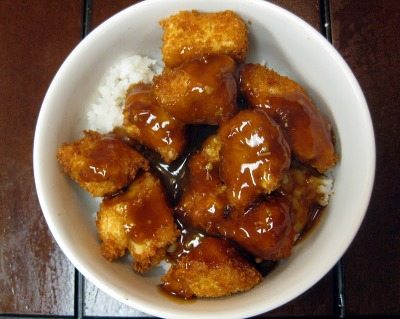 Top view of orange chicken in a white bowl with white rice.