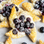 A puff pastry pinwheel topped with blueberries and powdered sugar.