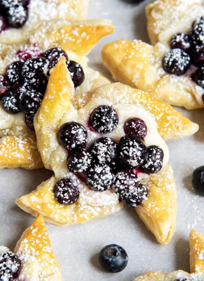 A puff pastry pinwheel topped with blueberries and powdered sugar.