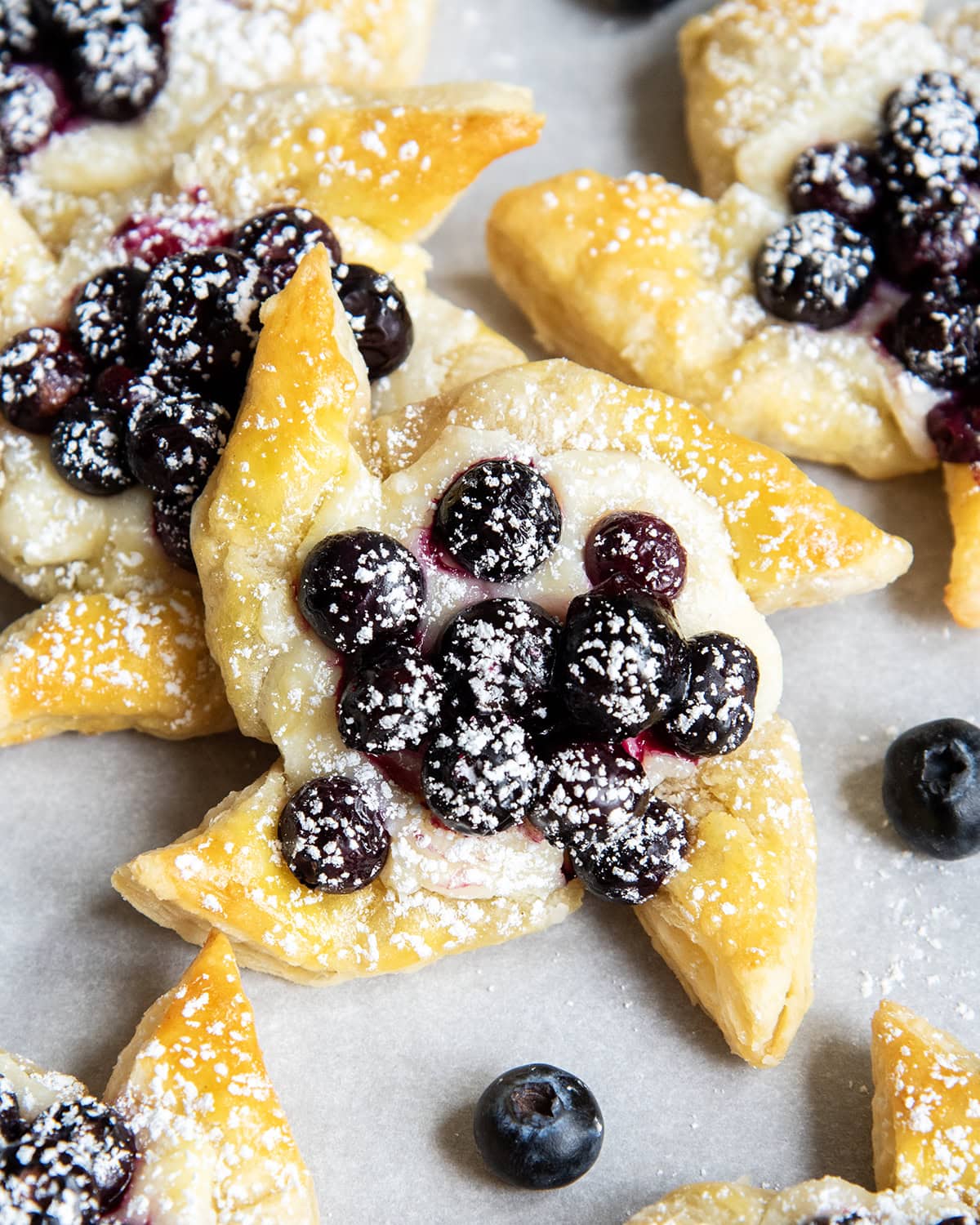 A puff pastry pinwheel topped with blueberries and powdered sugar.