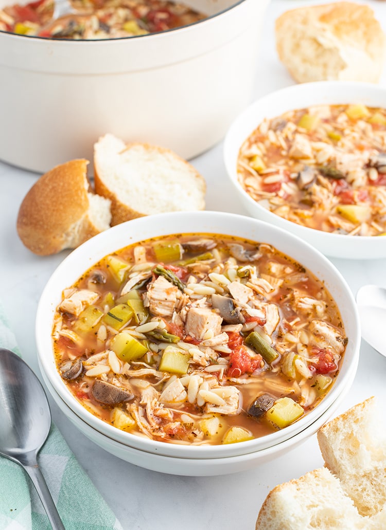 A bowl of turkey and orzo soup with french bread on the side.