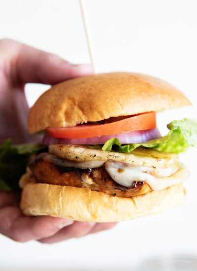 A hand holding a Hawaiian chicken sandwich, which has a chicken breast topped with cheese, tomato, and lettuce.