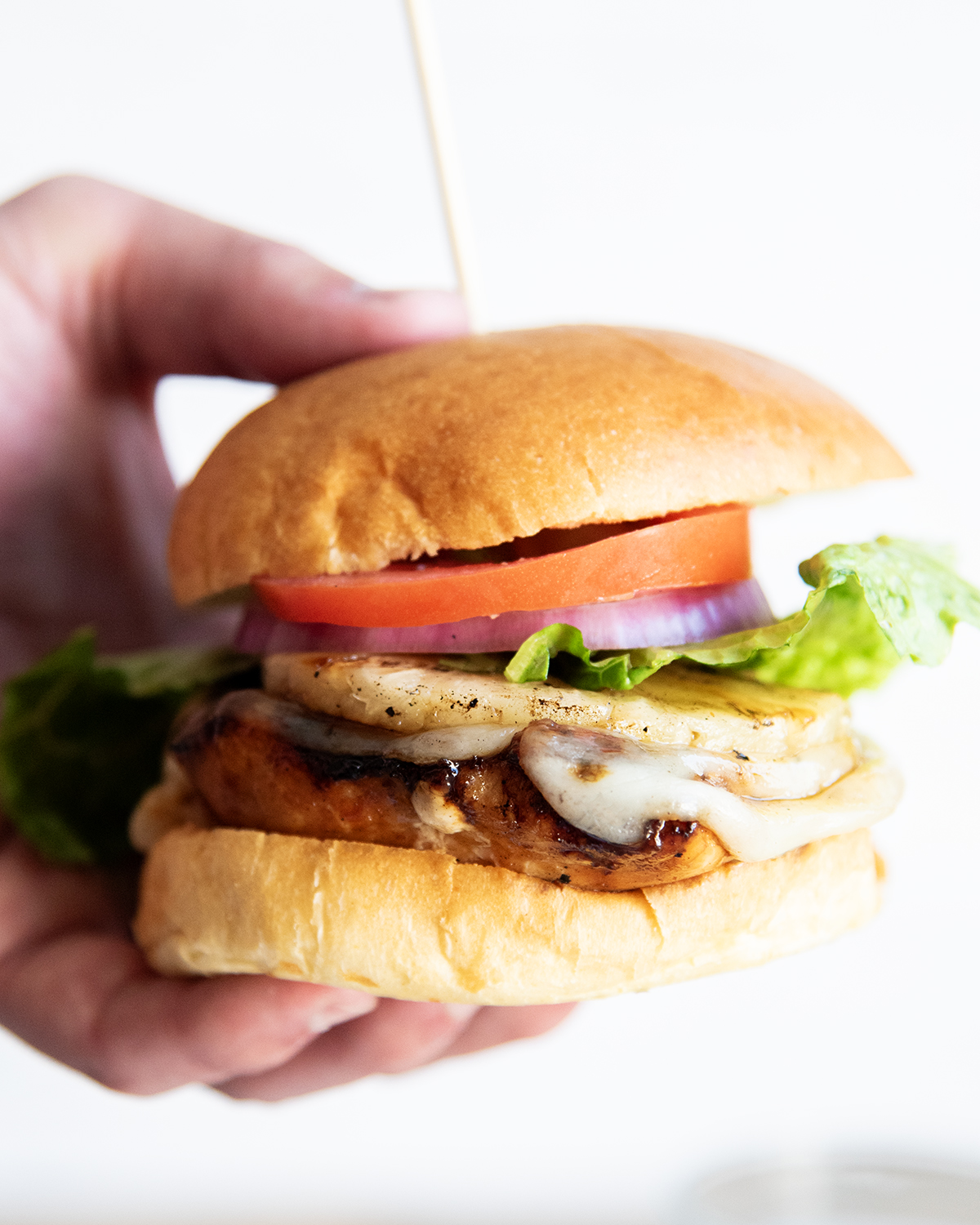 A hand holding a Hawaiian chicken sandwich, which has a chicken breast topped with cheese, tomato, and lettuce.