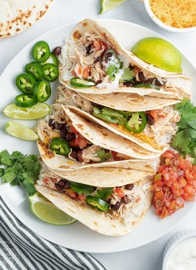 Above image of multiple crockpot chicken tacos with ingredients visible and white background on plate.
