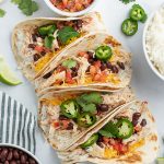Above image of multiple crockpot chicken tacos with ingredients visible and white background on plate.