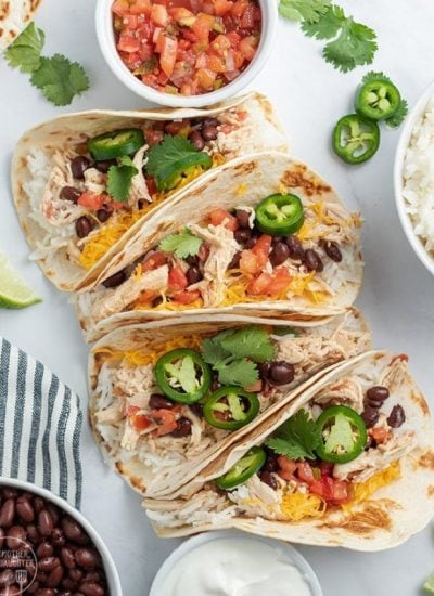 Above image of multiple crockpot chicken tacos with ingredients visible and white background on plate.