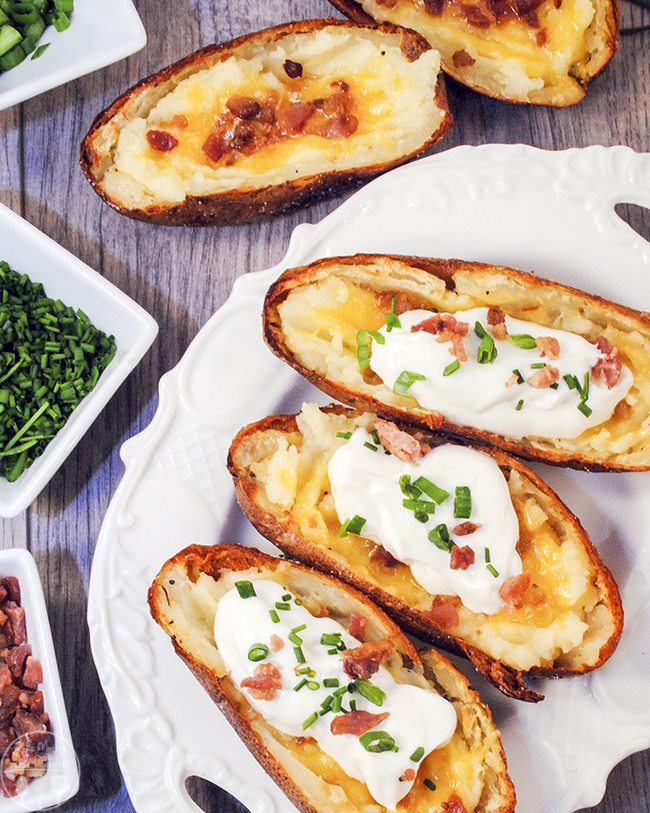 Three loaded potato skins on a white plate, topped with sour cream, chives, and bacon bits.