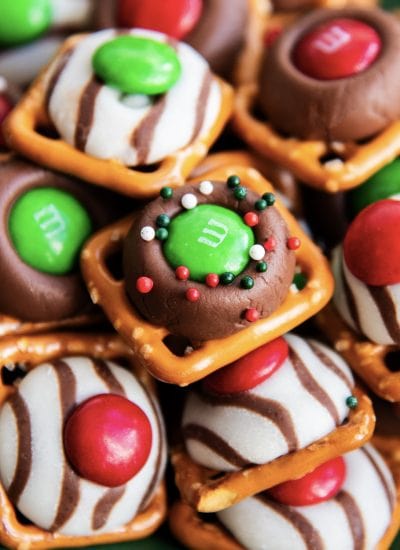 A close up of a pile of Christmas pretzel treats, with square snap pretzels, and topped with a green m&m and sprinkles.