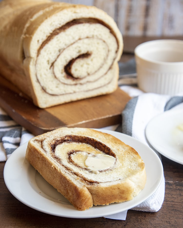 A slice of cinnamon swirl bread with butter on a white plate