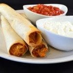 Front view of creamy chicken taquitos on a white plate with salsa and sour cream.