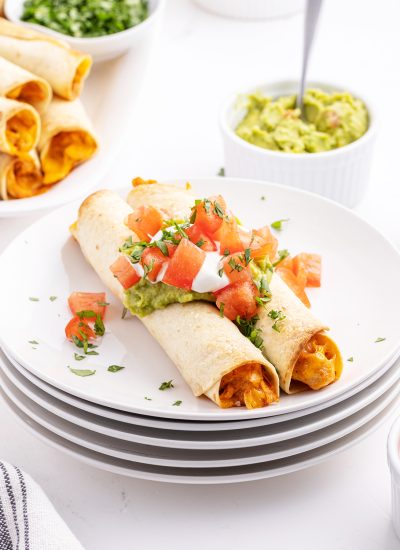 A plate of creamy chicken taquitos topped with guacamole and diced toamtoes.