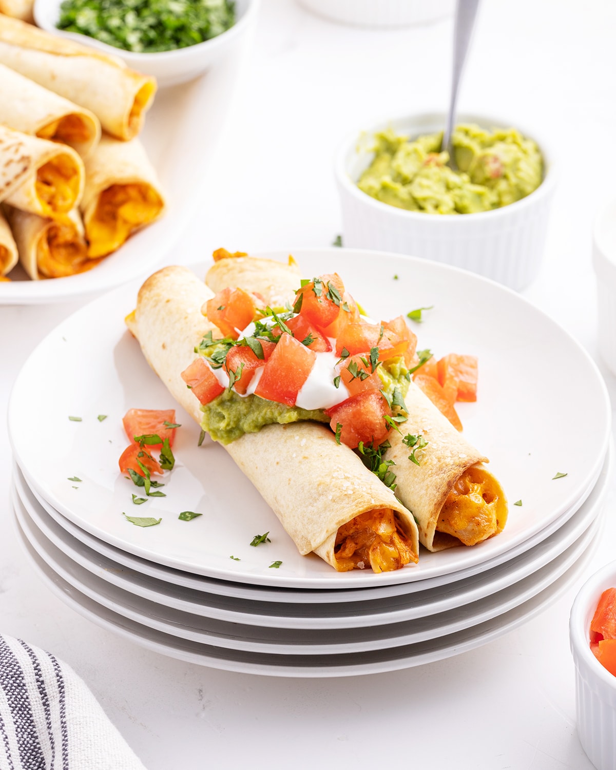 A plate of creamy chicken taquitos topped with guacamole and diced toamtoes.