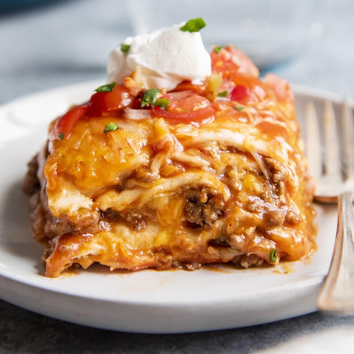 A square close up image of a slice of layered dutch oven enchiladas.