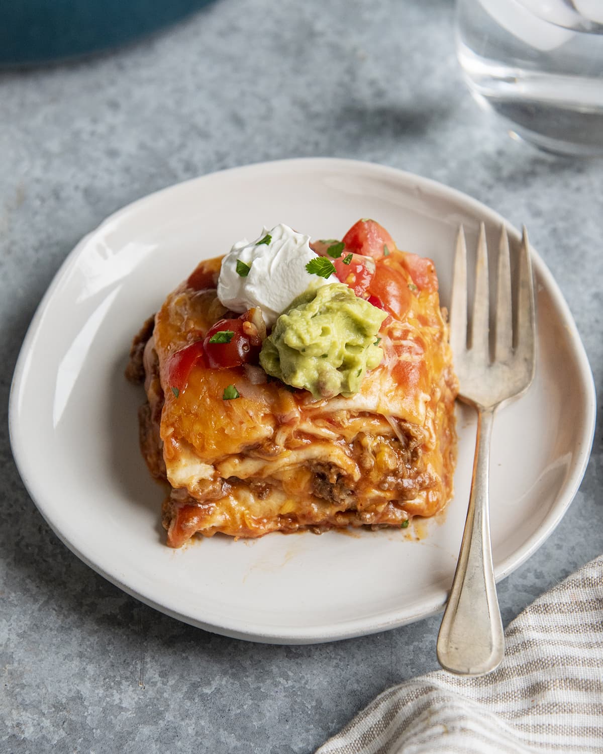 A plate of dutch oven enchilada casserole stack with sour cream and guacamole on top. 