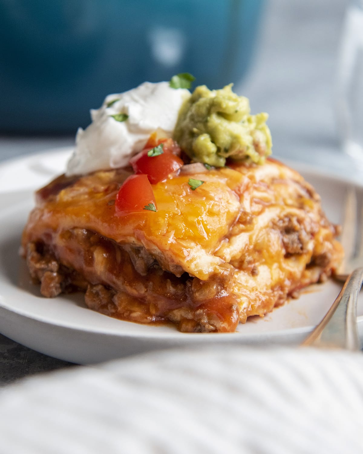 A close up of beef enchilada casserole topped with sour cream, salsa, and guacamole on a plate.