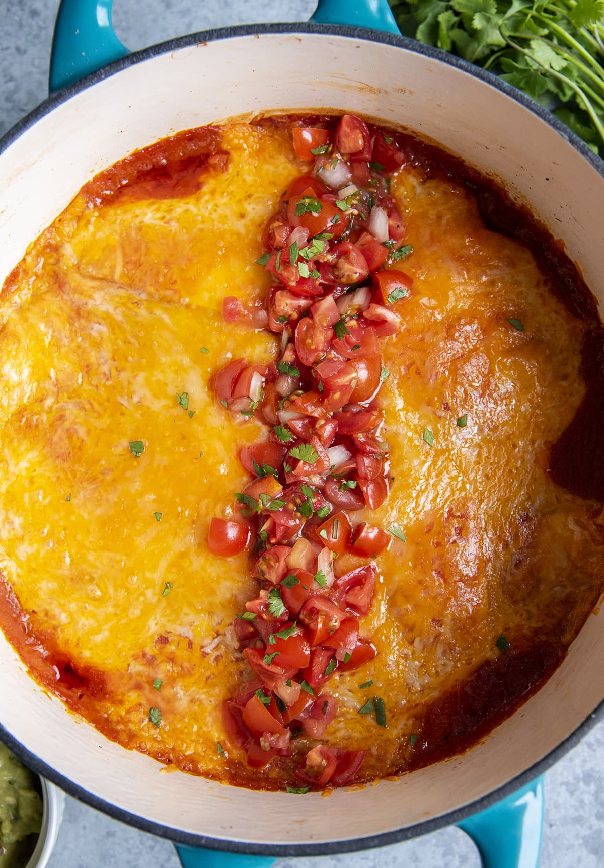 An overhead photo of dutch oven enchiladas topped with cheese and diced tomatoes.