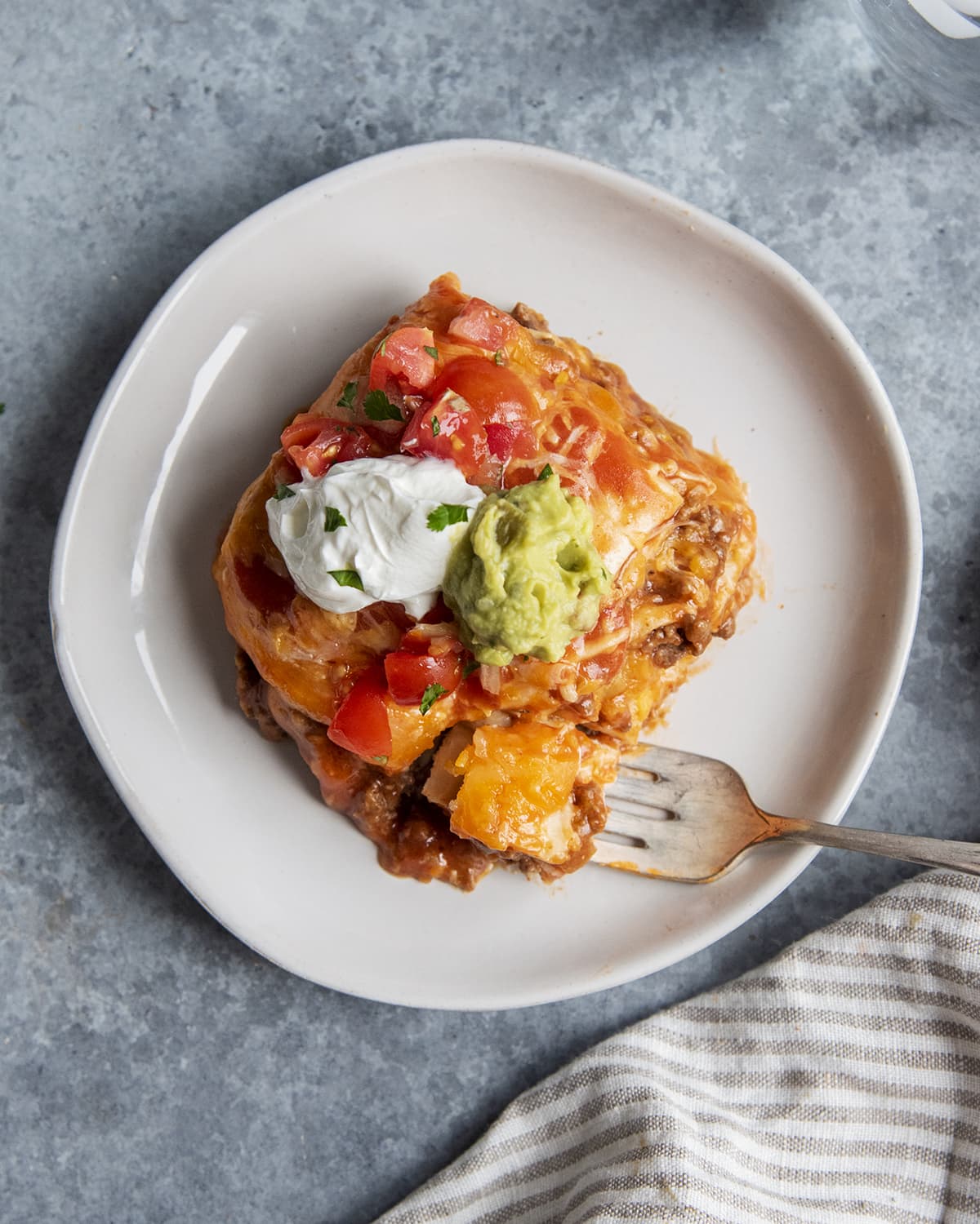 An overhead photo of a plate of beef dutch oven enchiladas topped with sour cream and guacamole.
