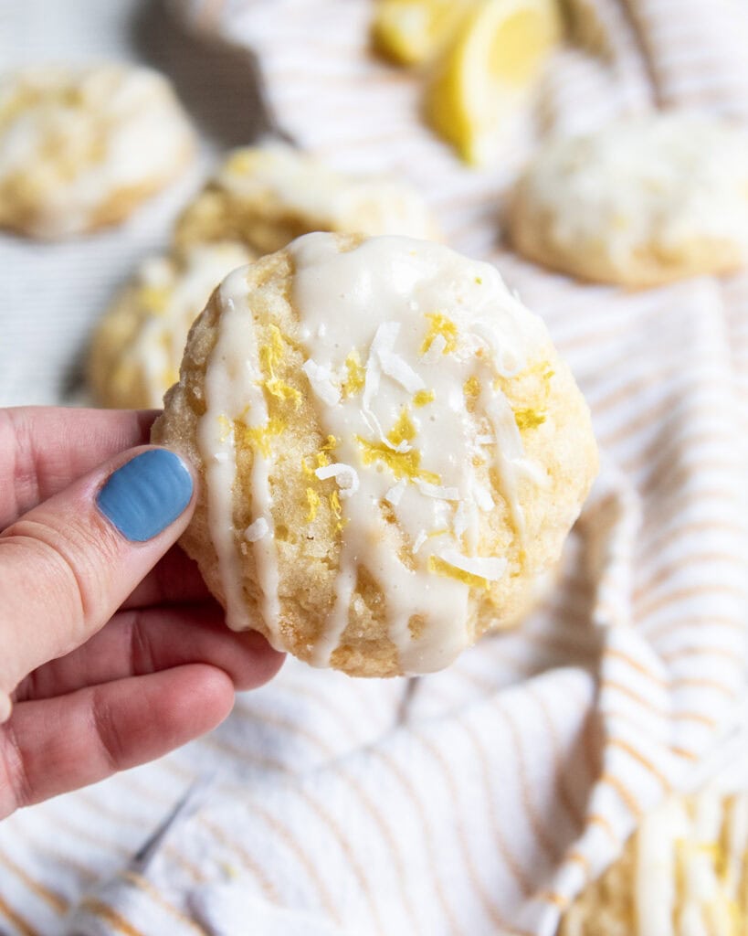 A hand holding a pineapple coconut cookie with a vanilla cream cheese glaze on top.