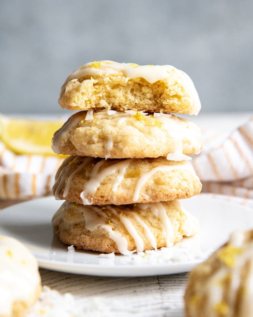 A stack of 4 thick cakey cookies on a plate, the top has a bite out of it showing the middle of the cookie.