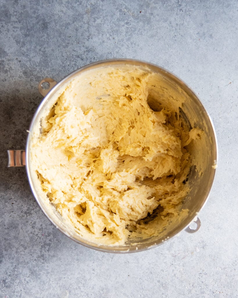 A stand mixer bowl with a yellow tinted cookie dough in it.