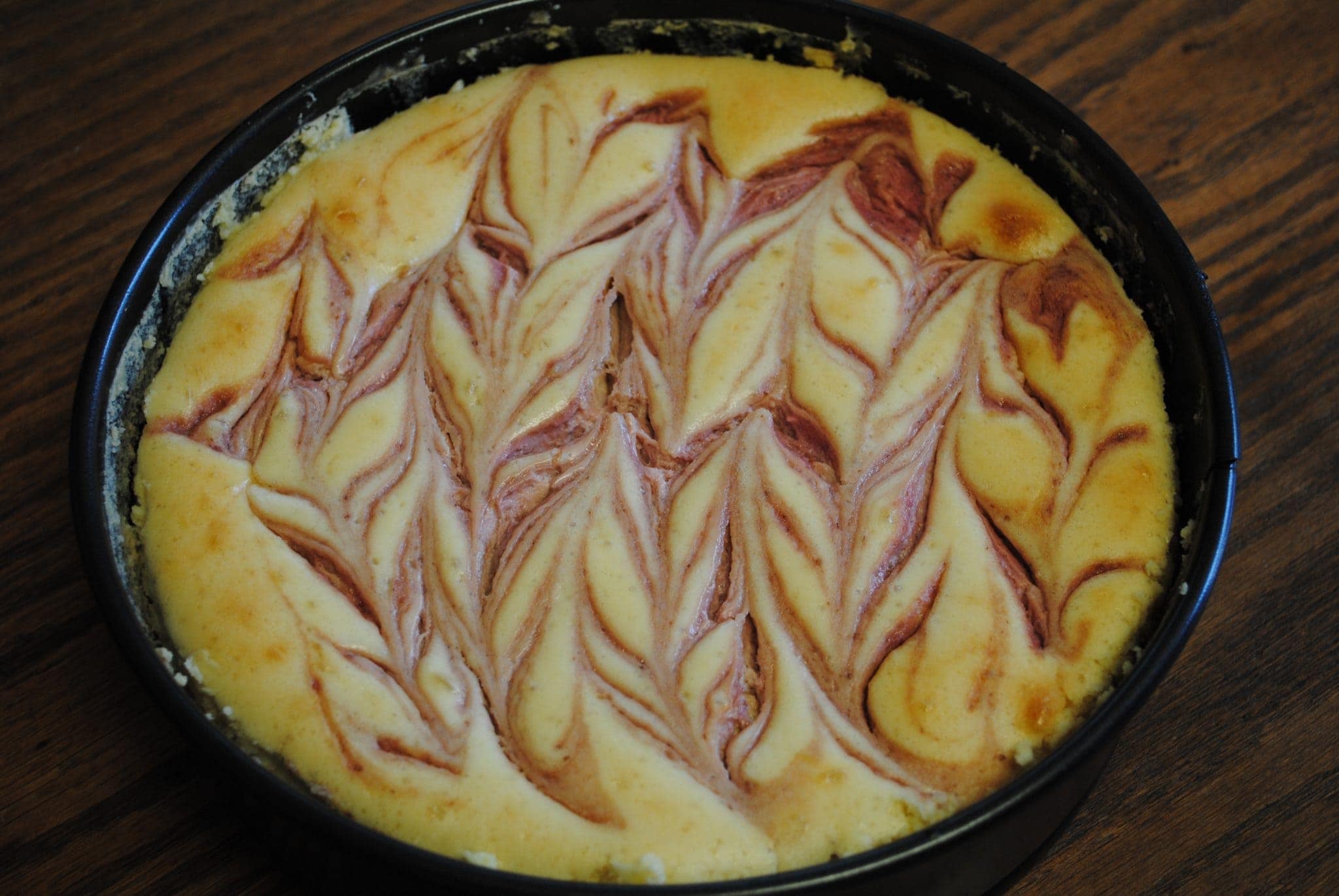 Top view of swirled strawberry and chocolate cheesecake in a baking pan.