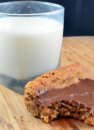Angled view of peanut butter bars on a wood board with milk.